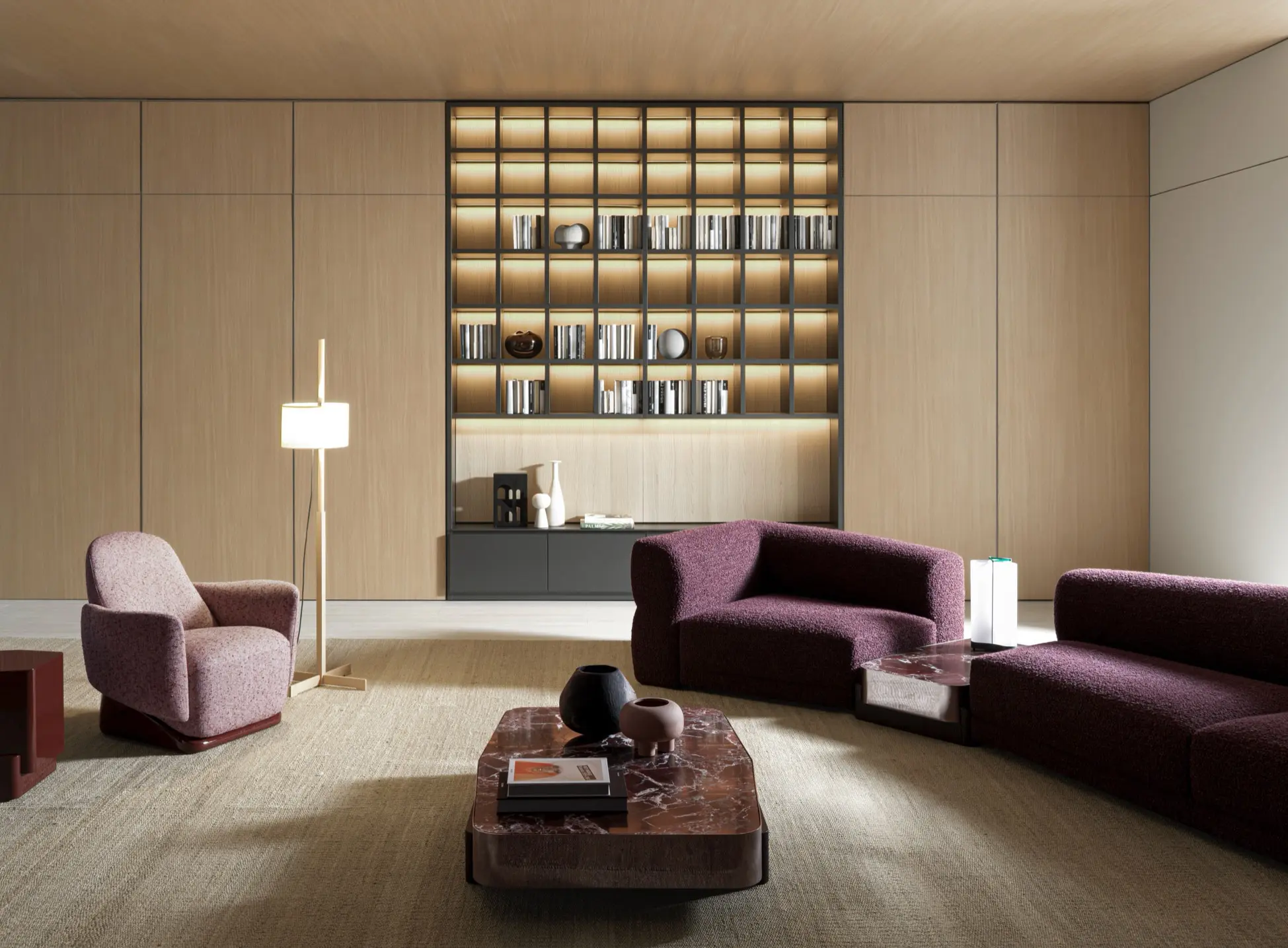 Soggiorno con pareti in legno chiaro, libreria a griglia retroilluminata, divano bouclé prugna e tavolino in marmo rosso